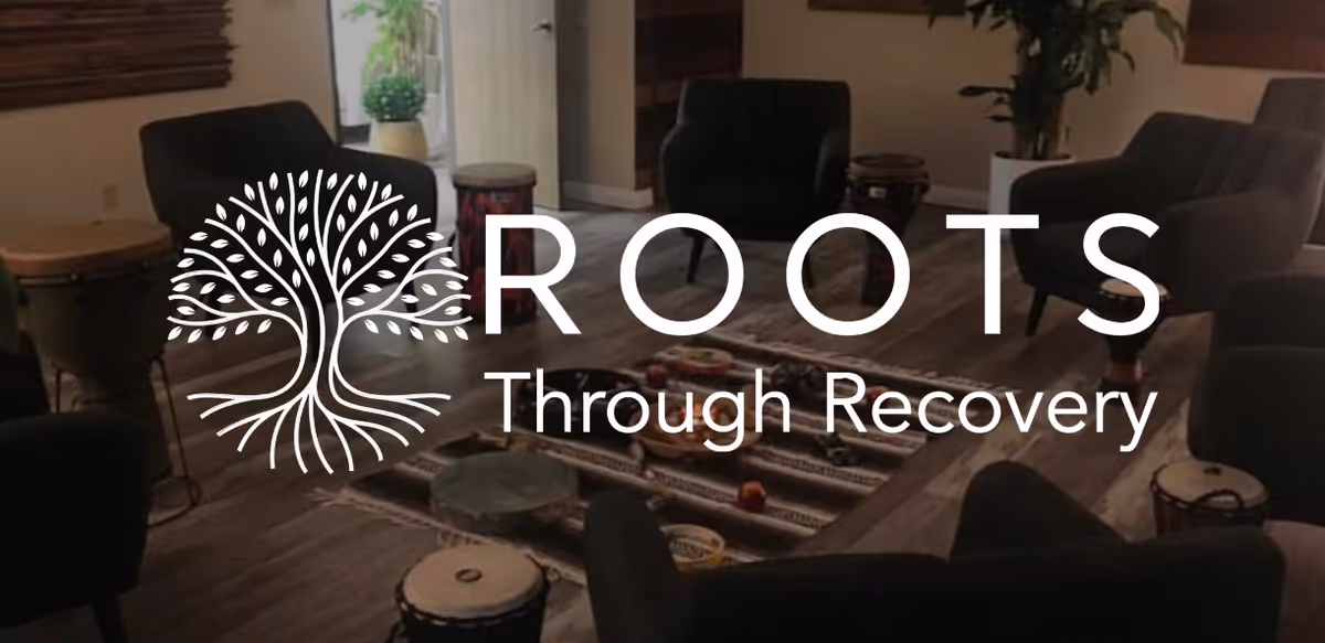 Indoor lounge with chairs around a coffee table and drums; branding overlay.