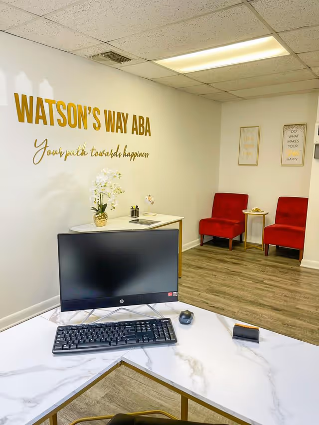 Reception area featuring Watson's Way ABA sign, computer desk, and red chairs.