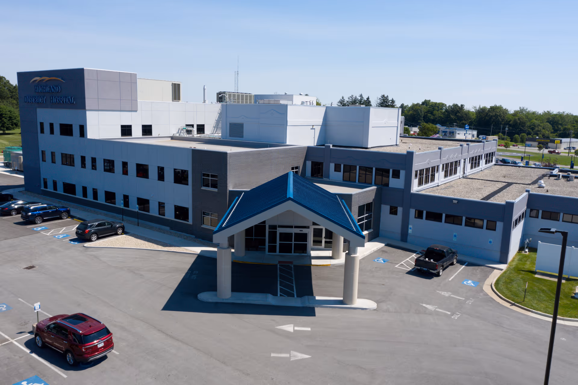 Exterior view of Highland District Hospital with a blue-roofed entrance and surrounding parking.