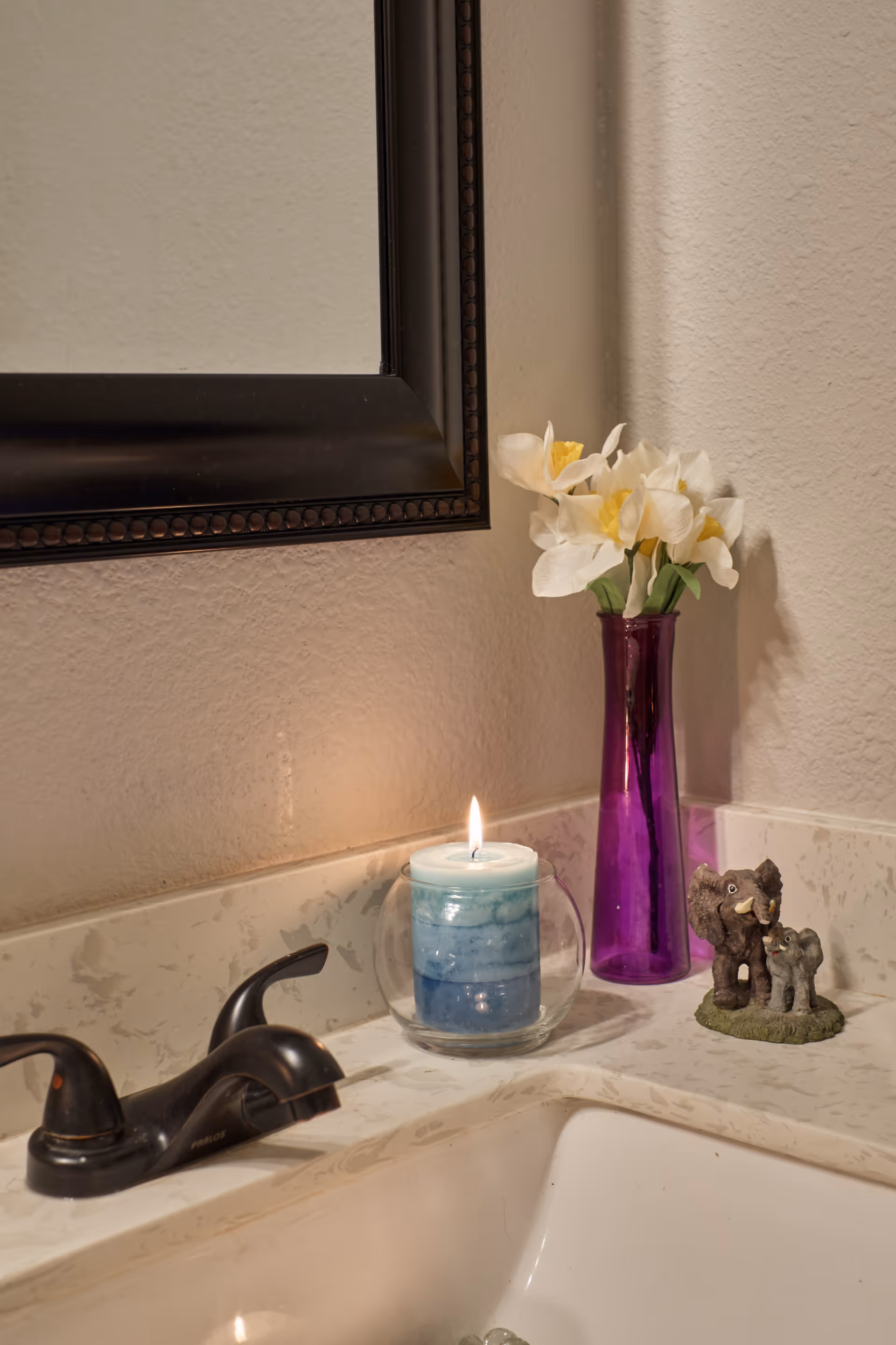 Bathroom sink area with candle, flowers in purple vase, and decorative cat figurines.