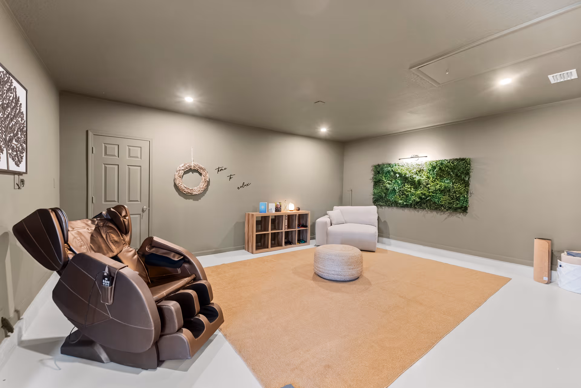 Basement-style lounge with a massage chair, sofa, wicker ottoman, and green wall art.