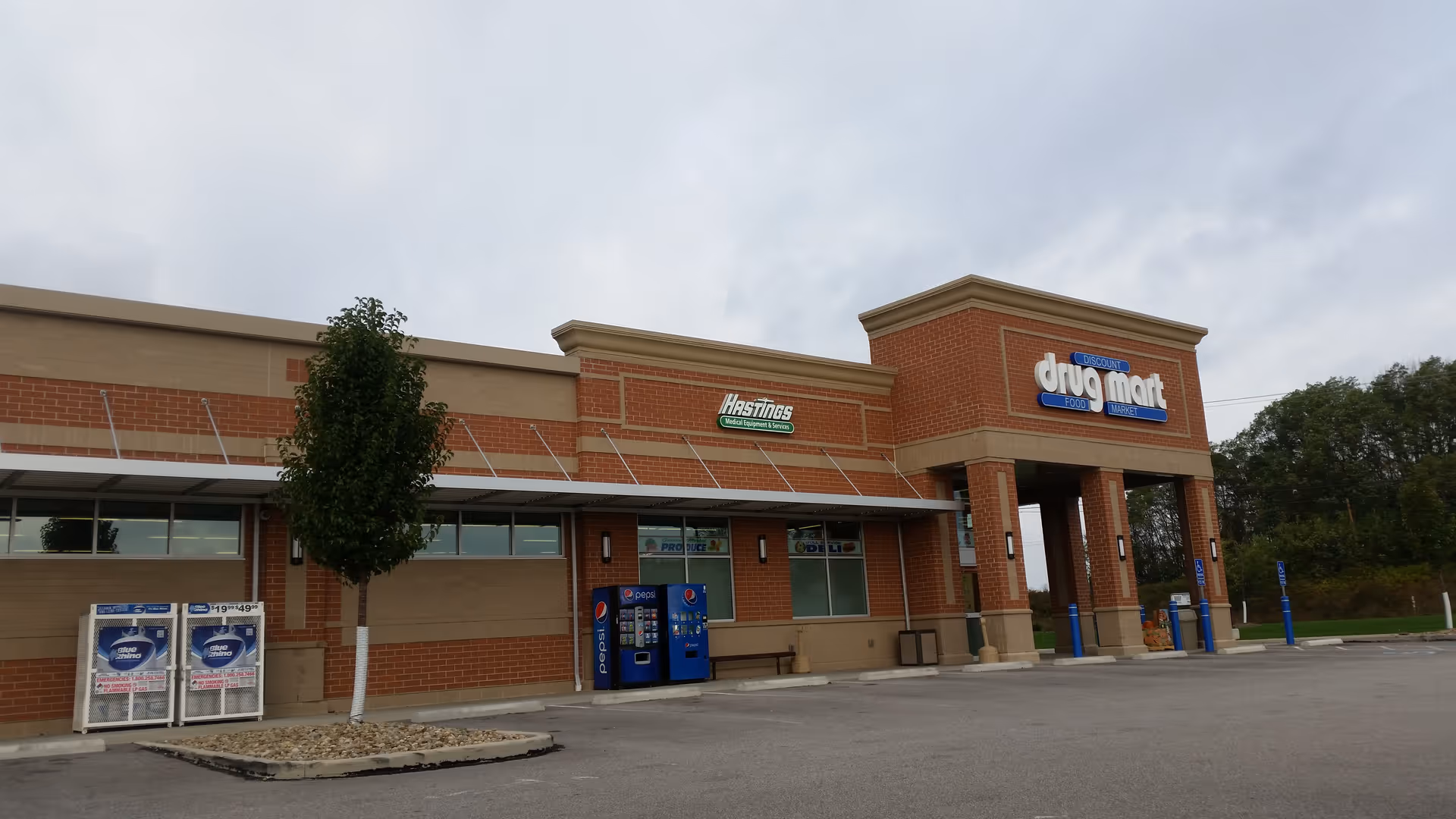 Brick Discount Drug Mart storefront with a parking lot, vending machines, and trees.