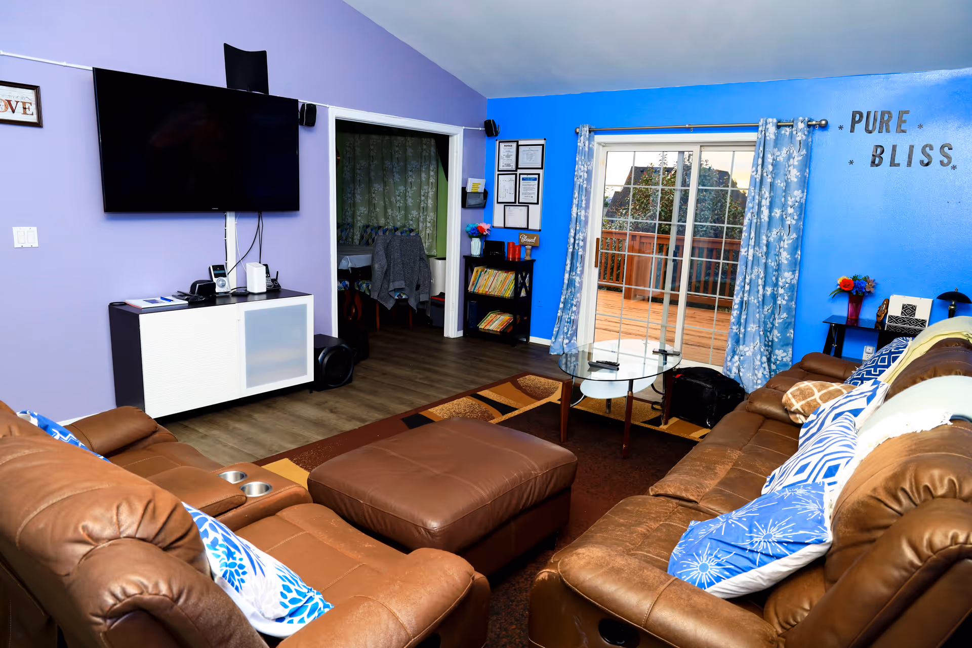 Bright living room with brown leather sectional, TV, and glass sliding doors to outdoor deck