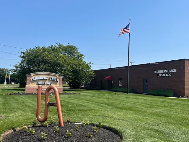 Exterior view of a brick building with a manicured lawn, sign, and waving American flag.