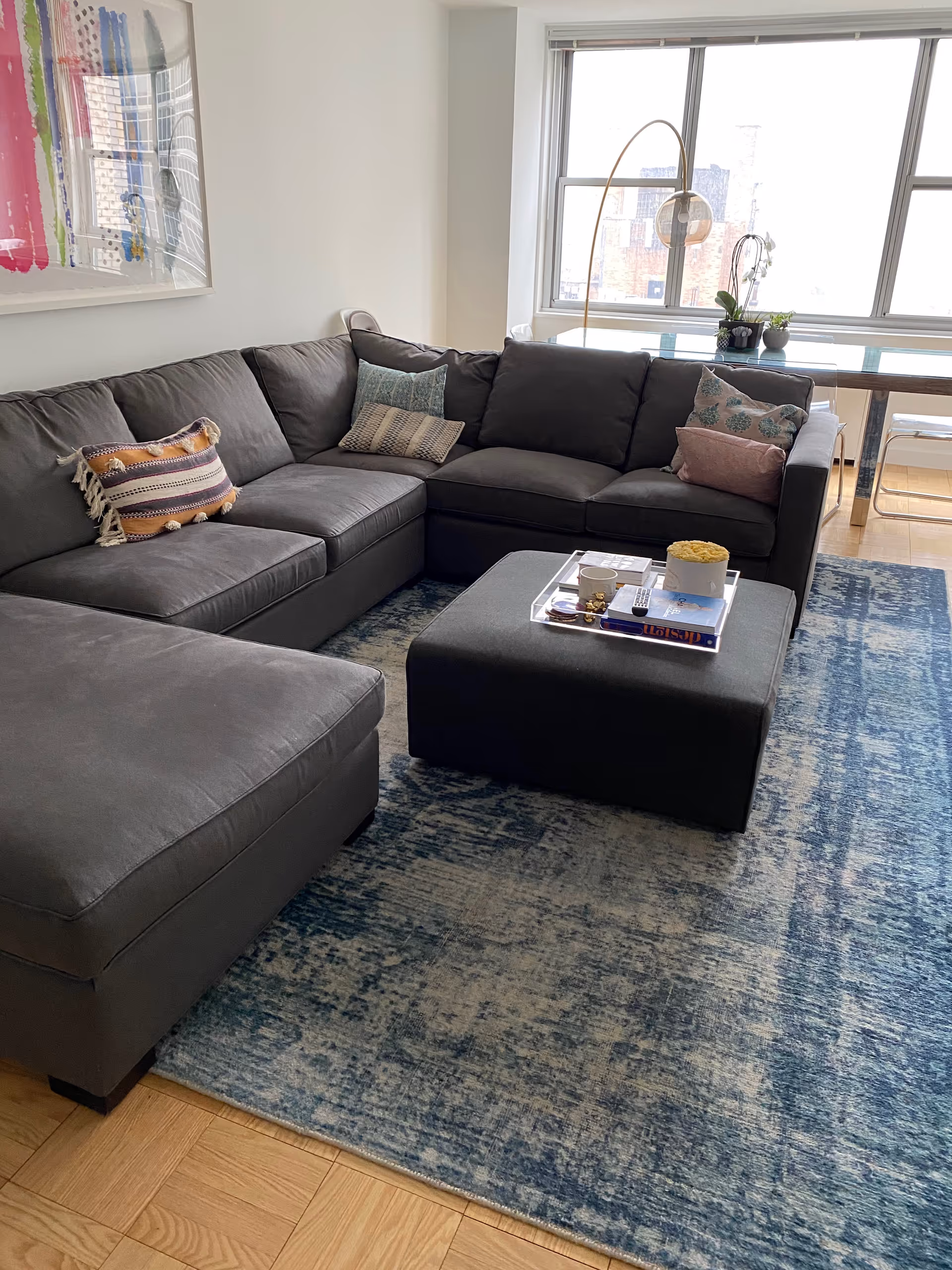 Modern gray sectional sofa with pillows sits in a bright living room by a window.
