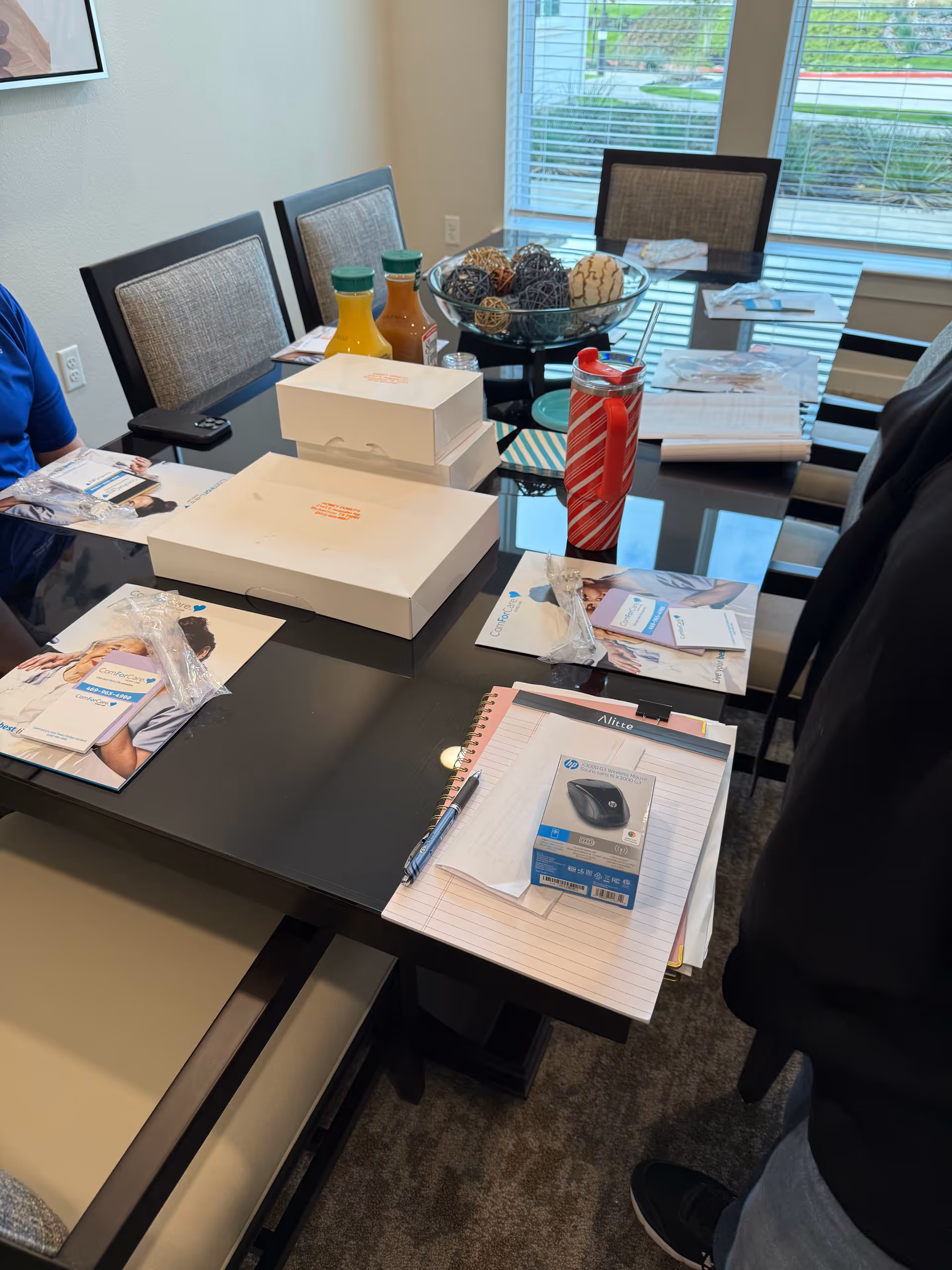 Meeting table with papers, boxes, drinks, and a decorative bowl in bright conference room.