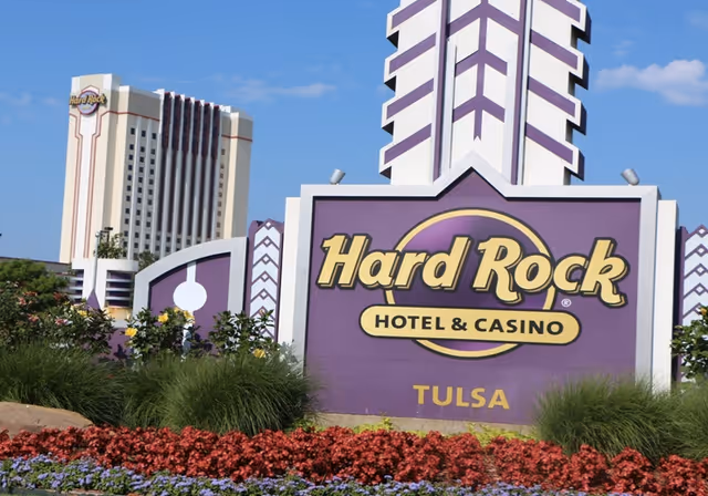Purple Hard Rock Hotel & Casino Tulsa sign with landscaping and blue sky.