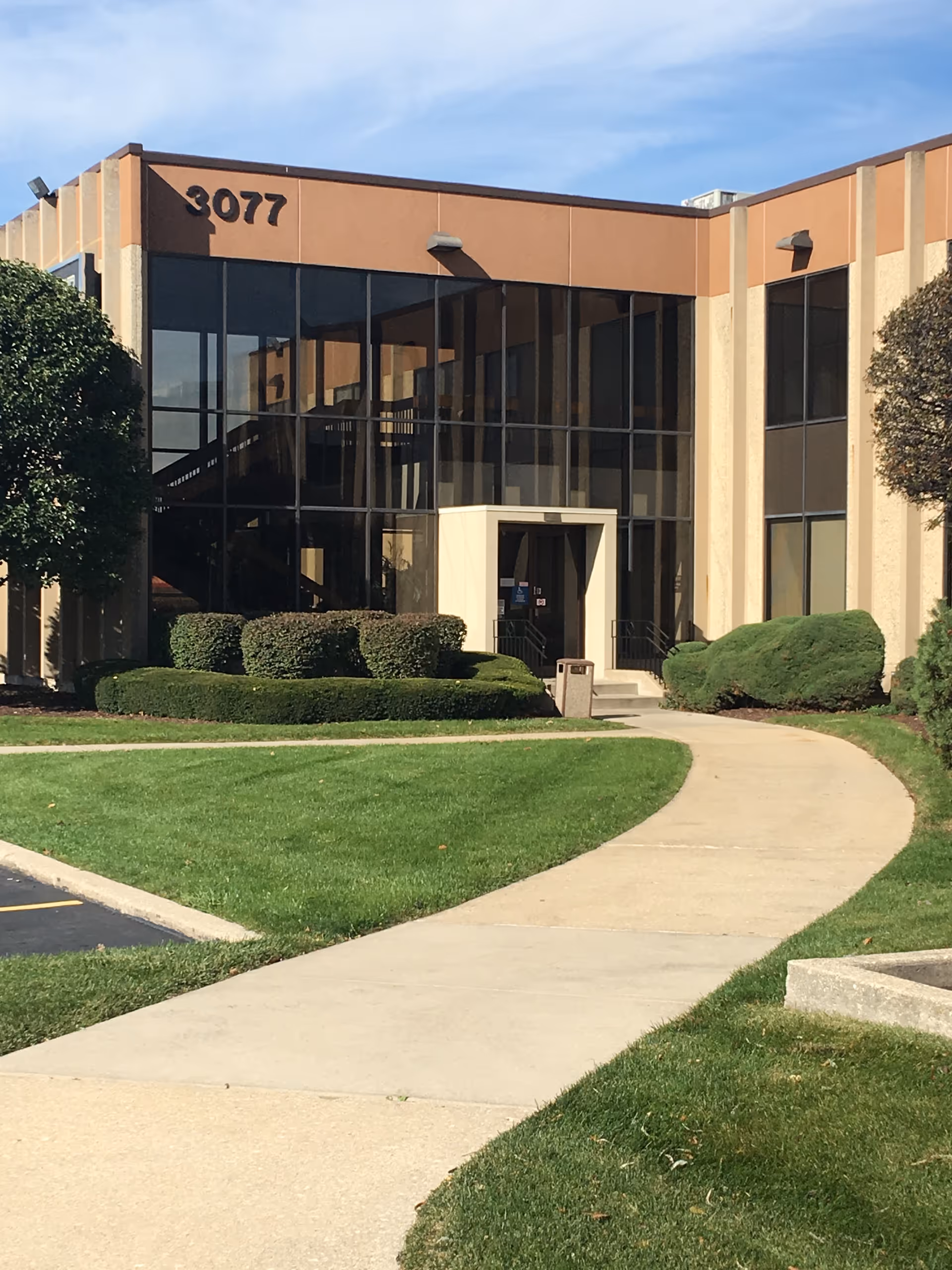 Front entrance of a tan, glass-front senior living building with a curved walkway.