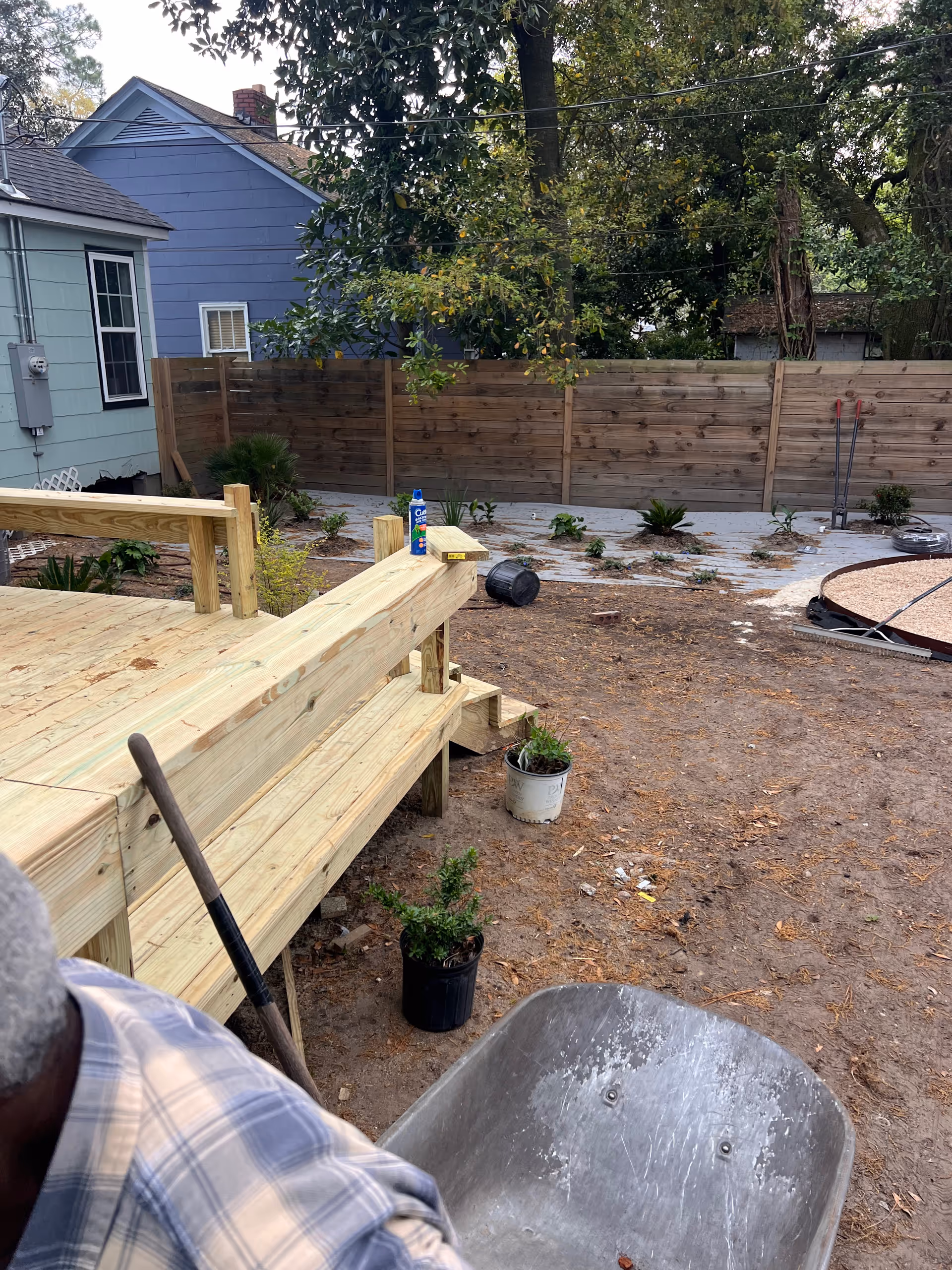 Backyard with a wooden deck under construction, wheelbarrow, potted plants, and a wooden fence