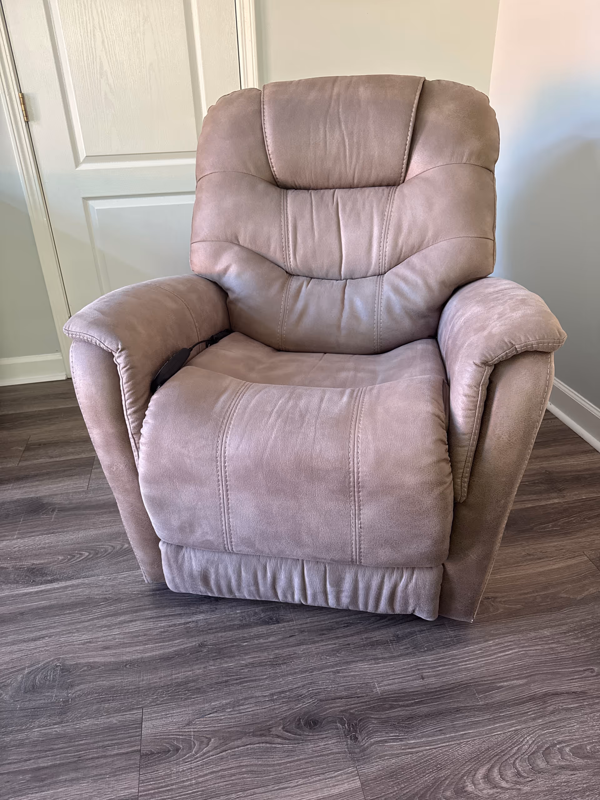 A plush pink recliner chair sits in a small, wood-floored living space.