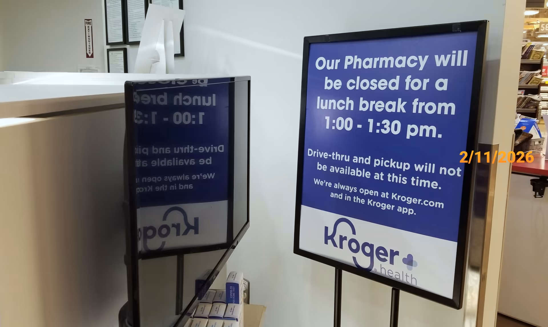 Blue Kroger Pharmacy sign on a stand inside a facility lobby.