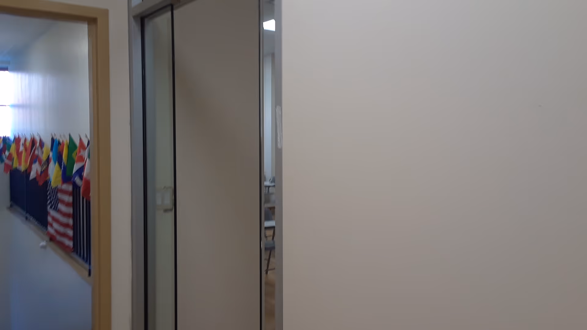 Interior hallway with glass doors and a row of colorful flags along the left wall.