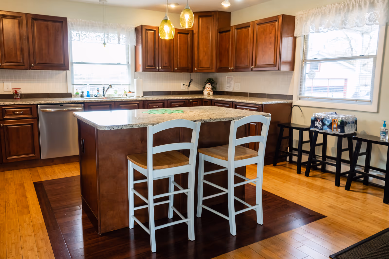 Modern kitchen with island, cabinets, sink, and two white stools in senior facility.