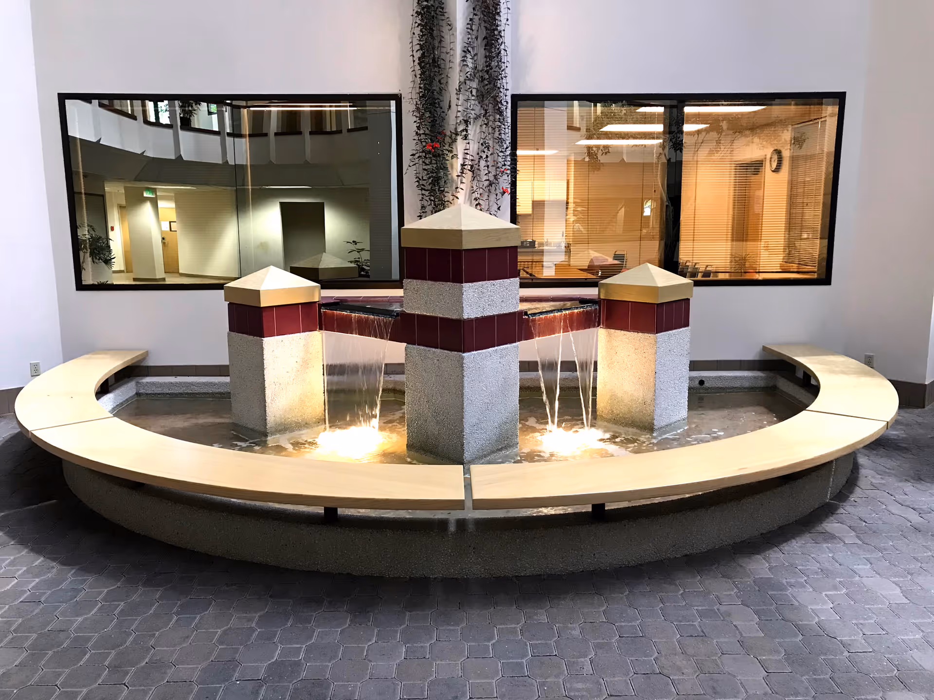 Circular seating surrounds a three-pillar fountain in a modern indoor lobby.