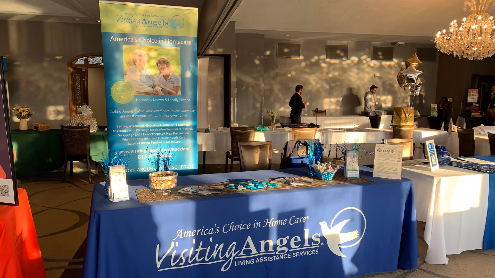Indoor event space with Visiting Angels banners, tables, and staff present in a banquet hall.
