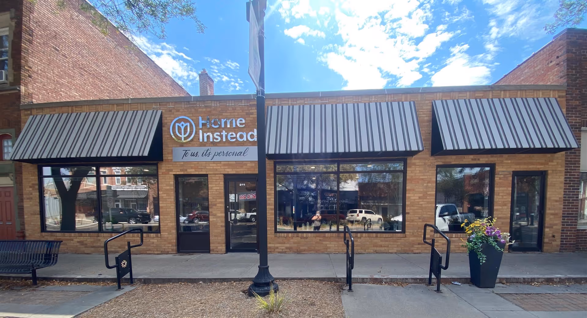 Brick storefront with three black awning canopies, Home Instead sign, large front windows, and sidewalk.