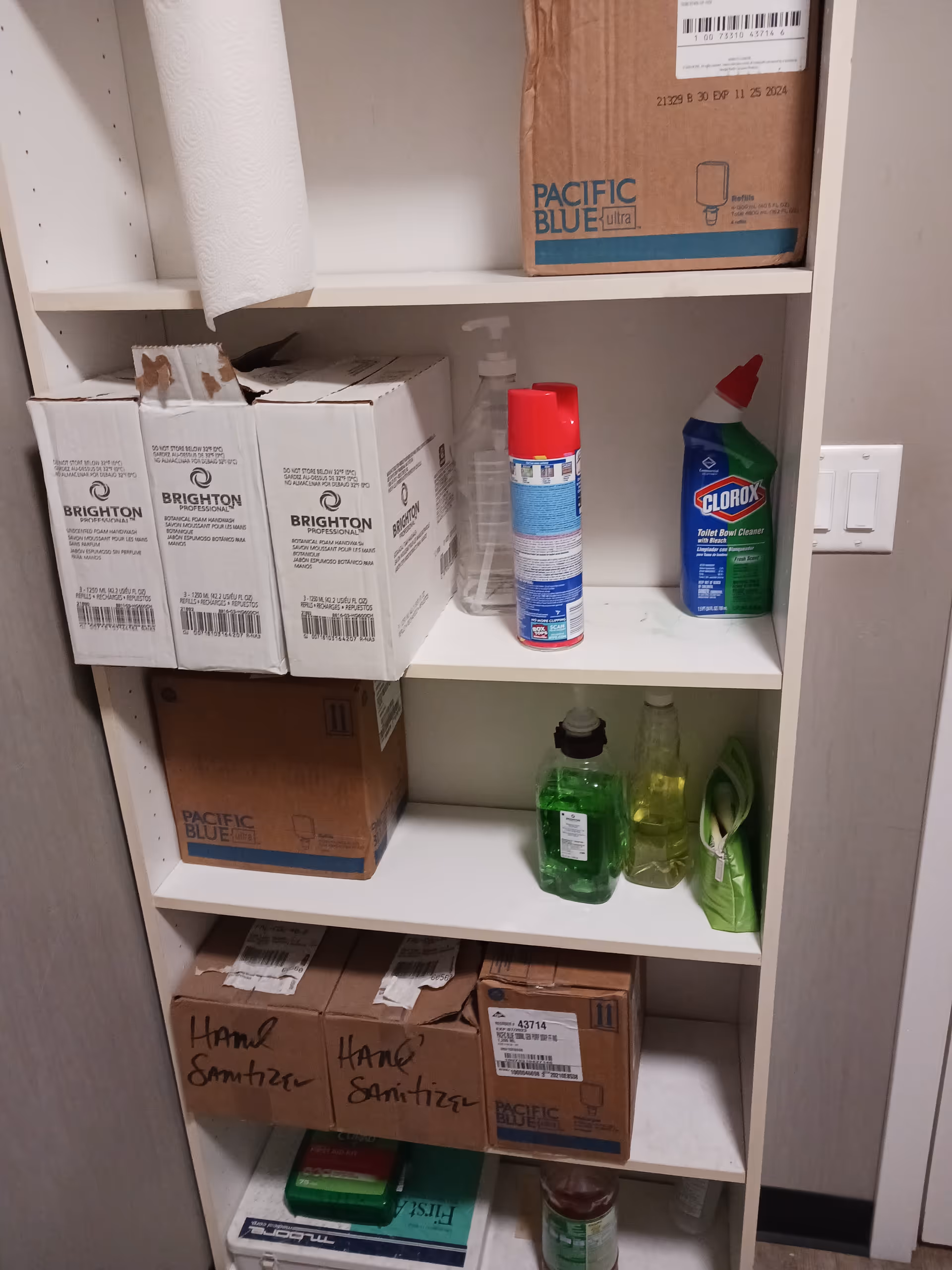 Shelves stocked with cleaning supplies and cardboard boxes in a utility storage cabinet.