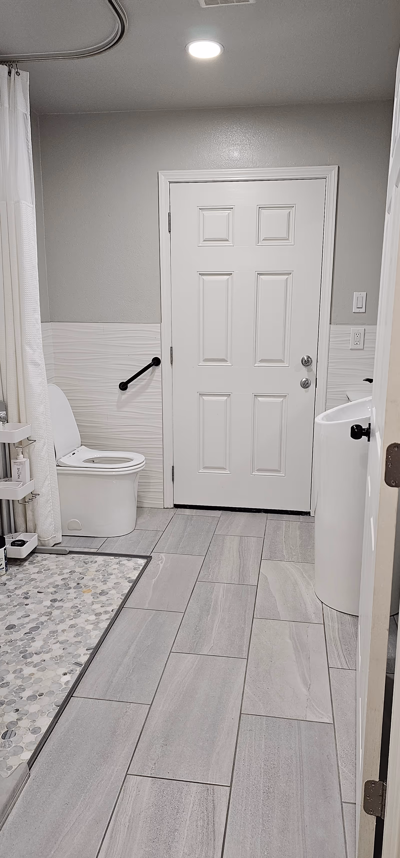 Modern bathroom in a senior living facility with toilet, sink, shower curtain, and grab bar.