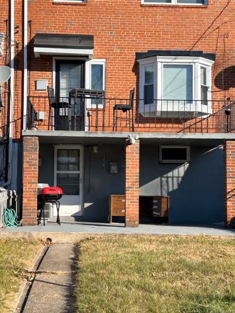 Brick apartment building exterior with a ground-level patio, grill, and balcony seating.