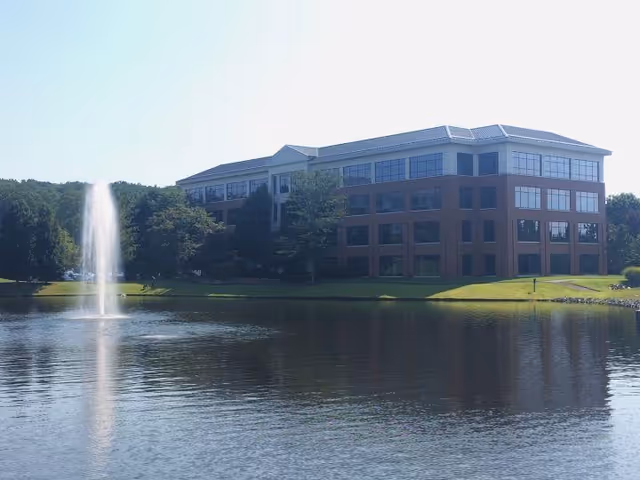 Exterior view of a brick building beside a pond with a fountain.