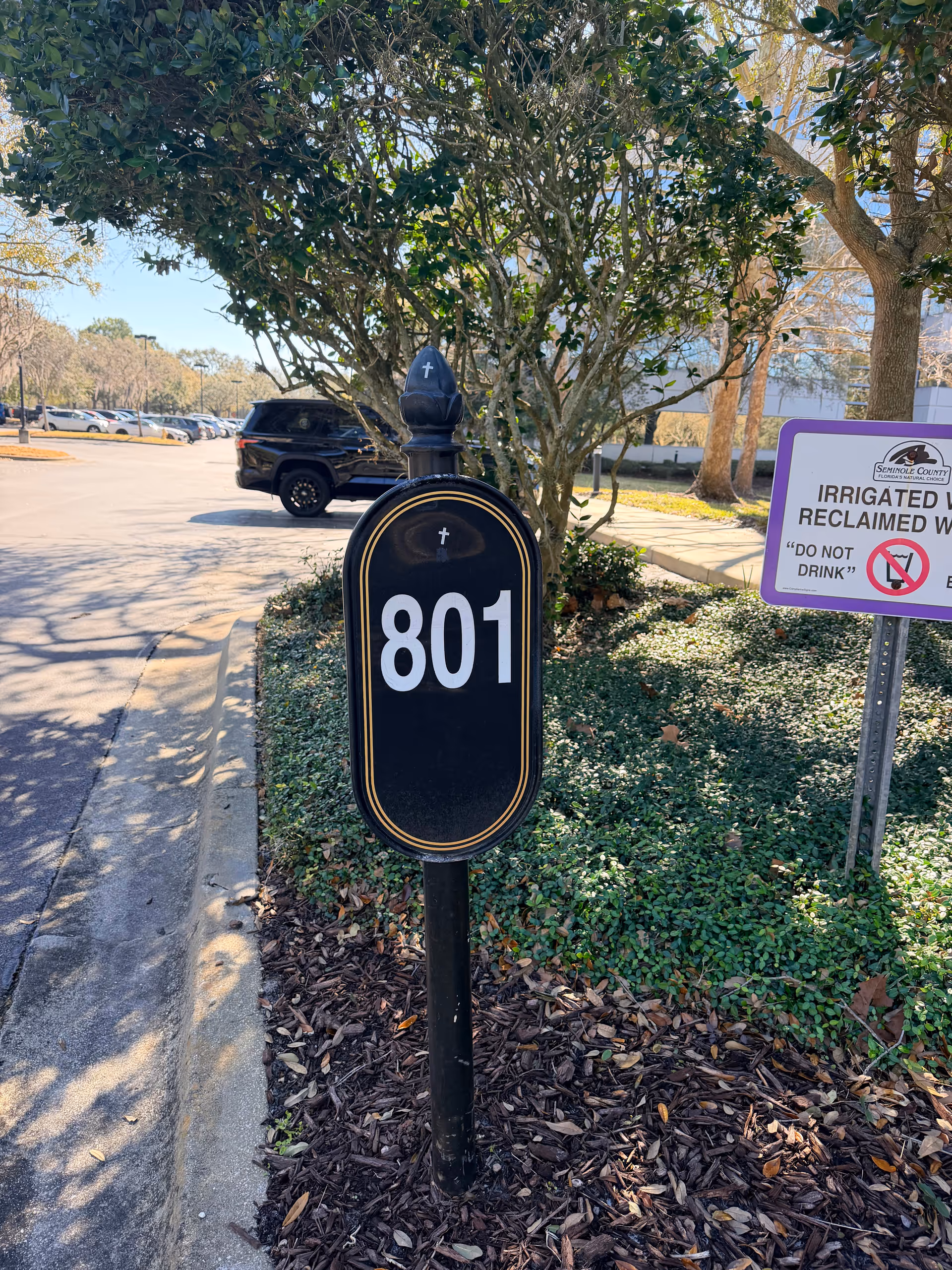 Exterior scene with a black 801 mailbox beside an irrigated reclaimed water sign among shrubs.