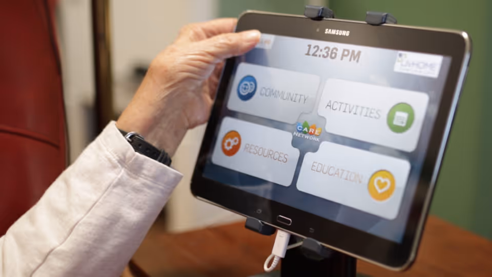 A hand holds a Samsung tablet displaying community, activities, resources, and education icons.