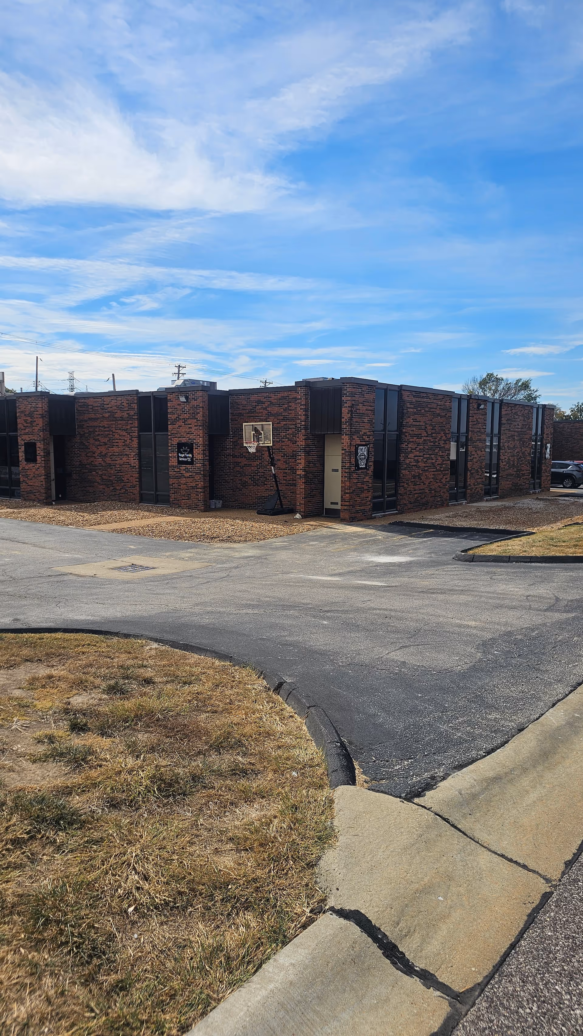 Brick, single-story facility exterior with multiple units, parking lot, and bright blue sky.