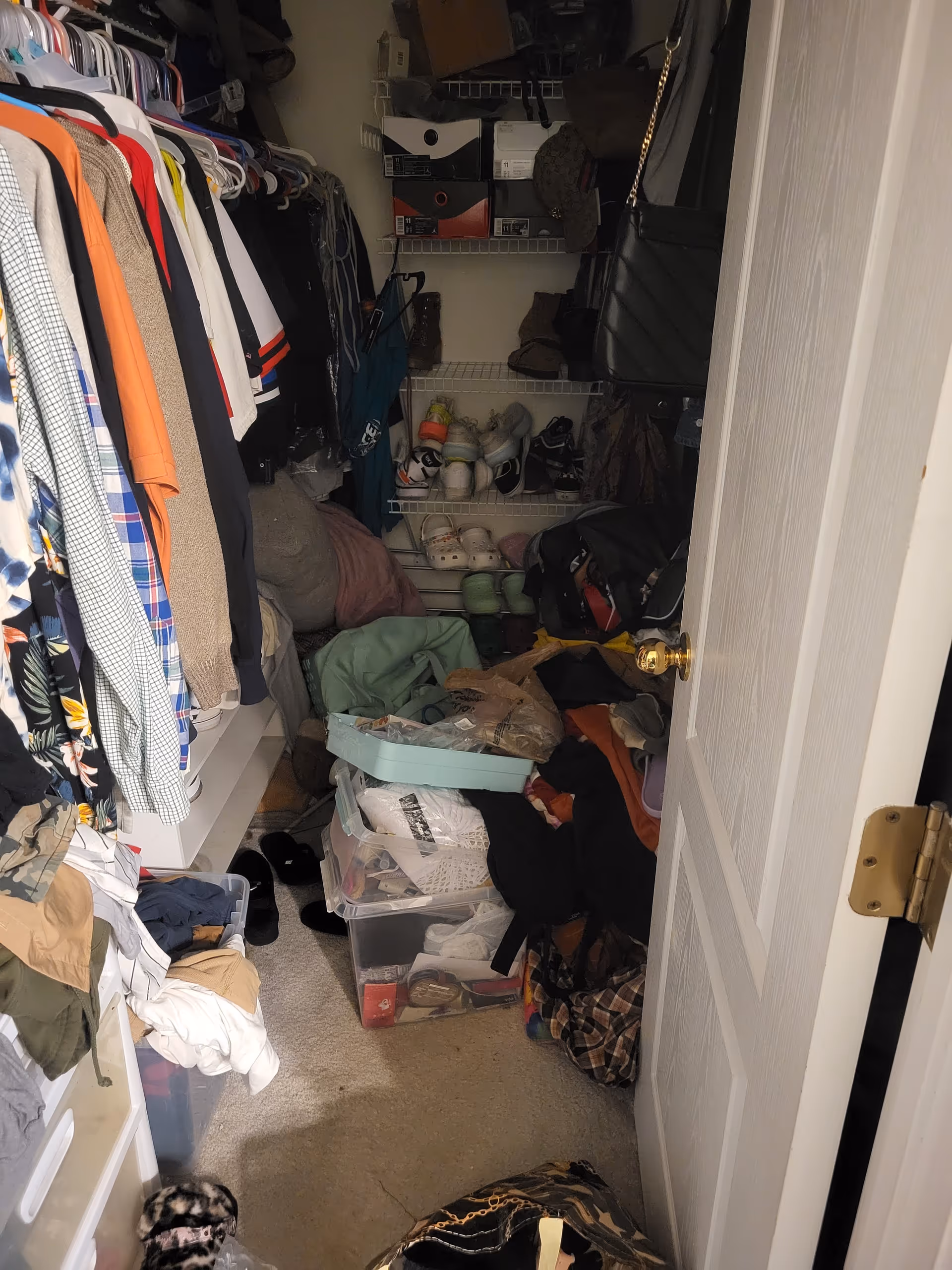 Cluttered closet filled with hanging clothes, shoes, and storage bins.
