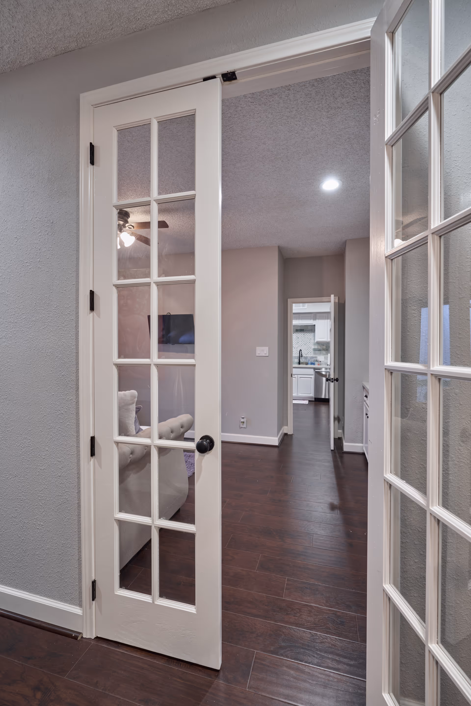 Glass-paneled French door opens to a living room with couch and TV.