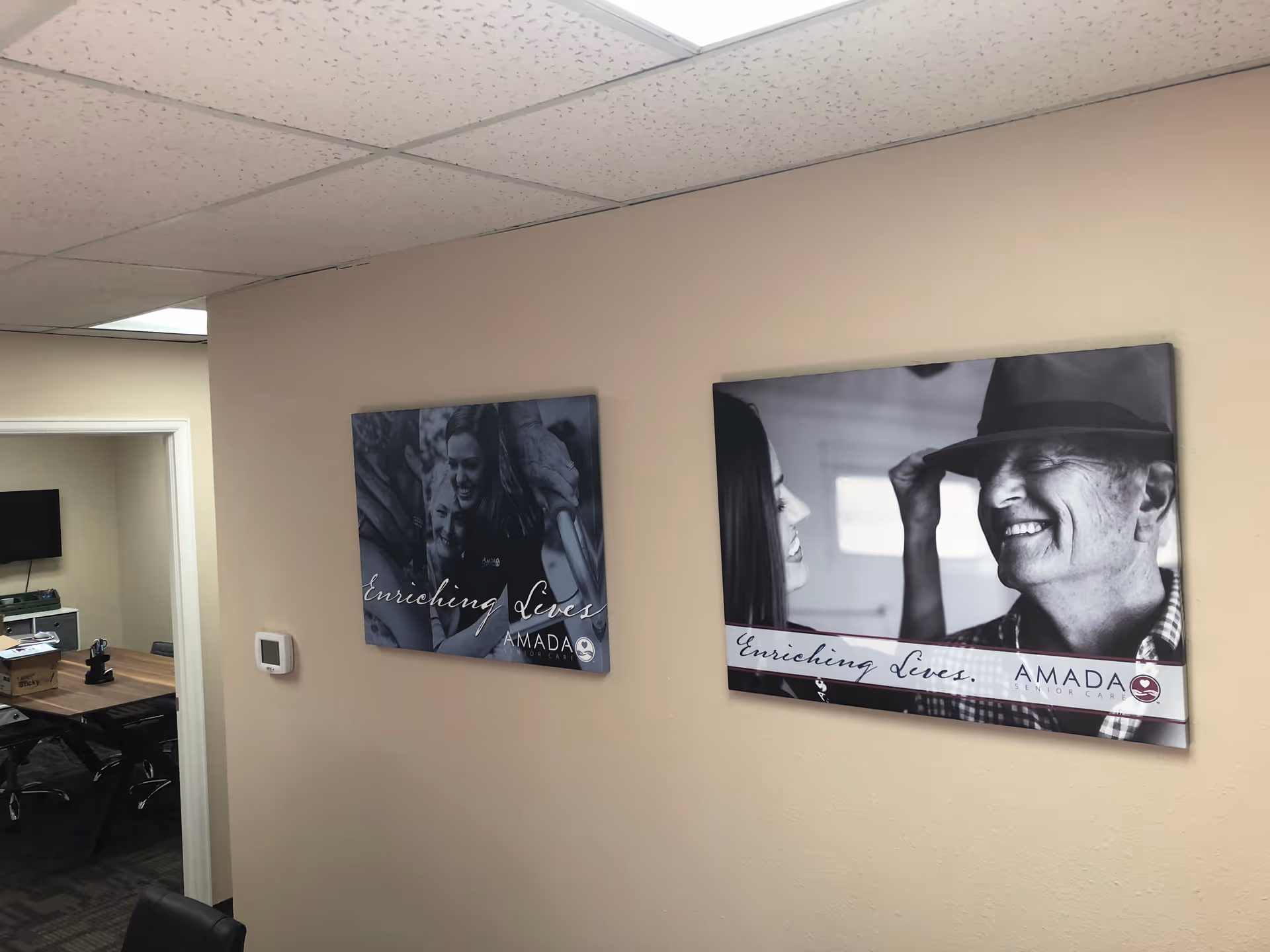 Interior hallway of Amada Senior Care with wall posters and a doorway to a conference room.