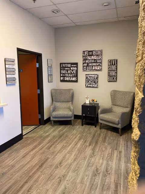 A small hospice lobby waiting area with two gray armchairs, a side table, and wall art.