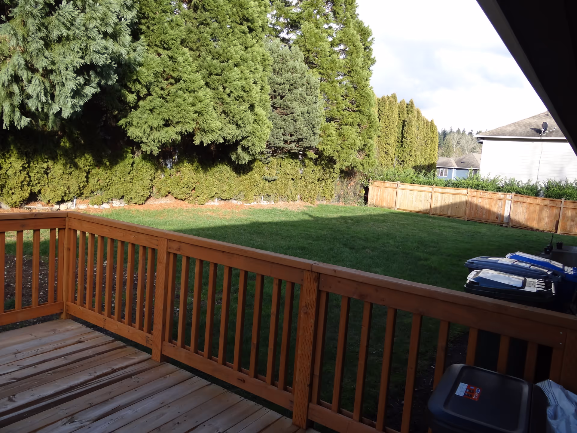 Backyard view from a wooden deck showing lawn, trees, and a fence.