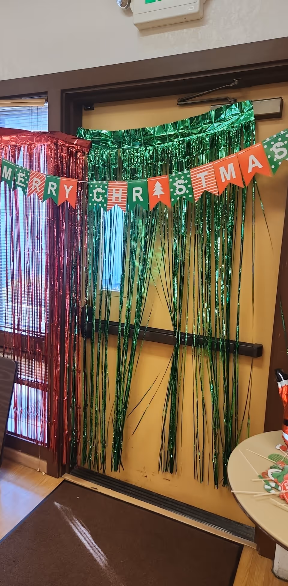 Green and red metallic fringe curtains decorate an indoor doorway with a Merry Christmas banner.