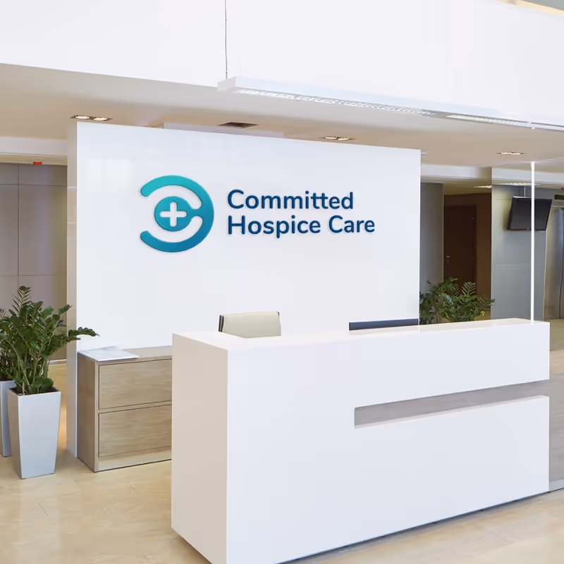 Bright lobby with white reception desk and 'Committed Hospice Care' logo sign.