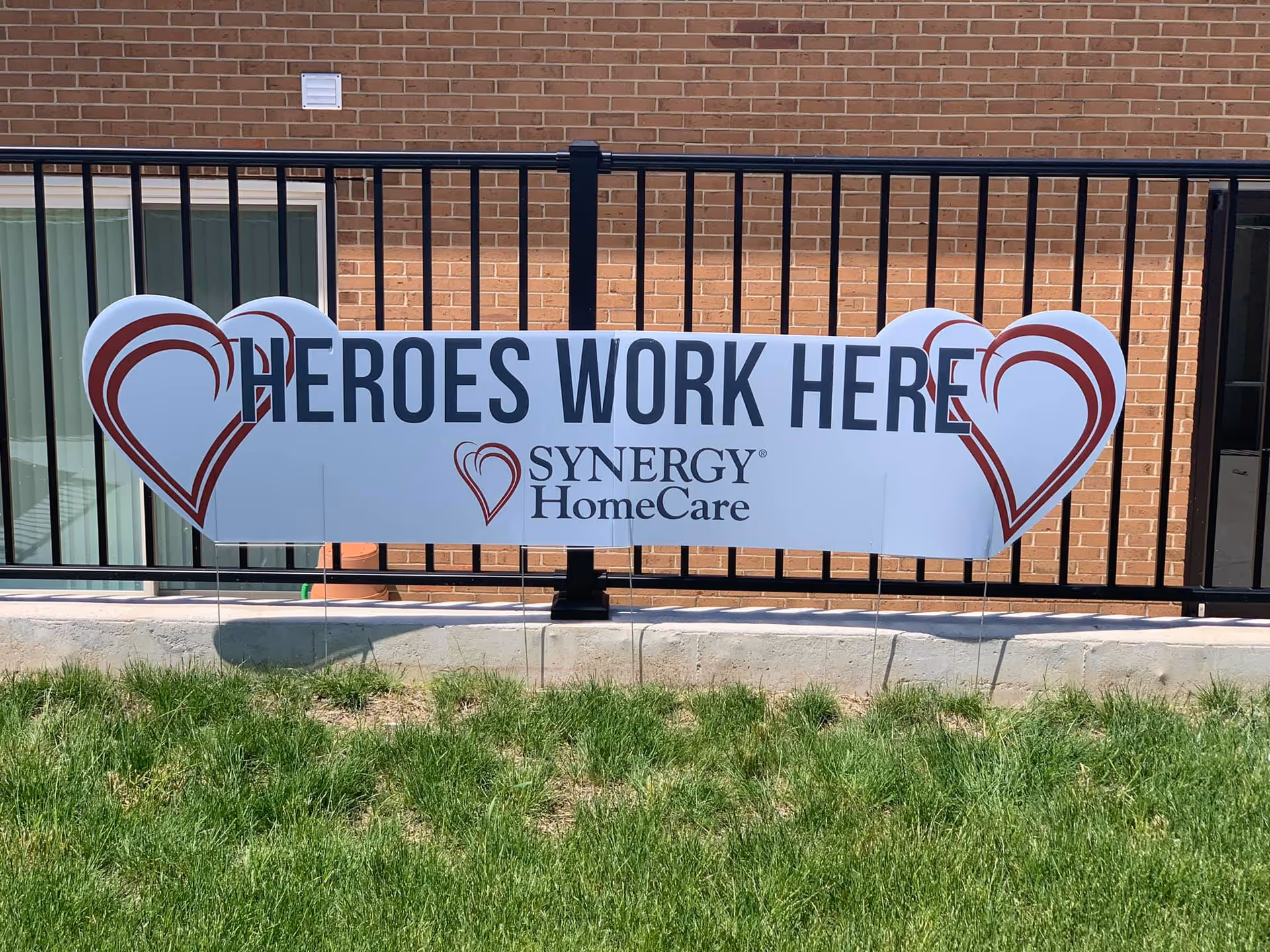 Banner reading Heroes Work Here for Synergy HomeCare attached to railing in front of brick building