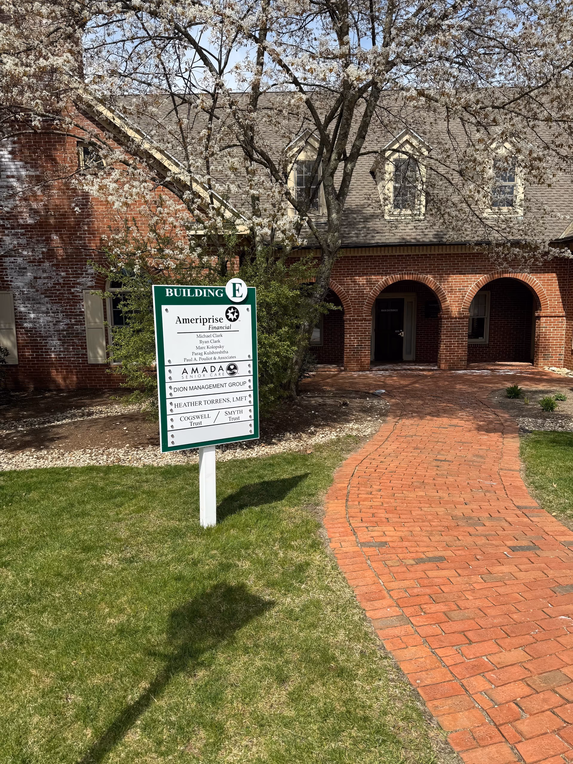 Brick building with arched entry, brick walkway, and a green sign in front yard.