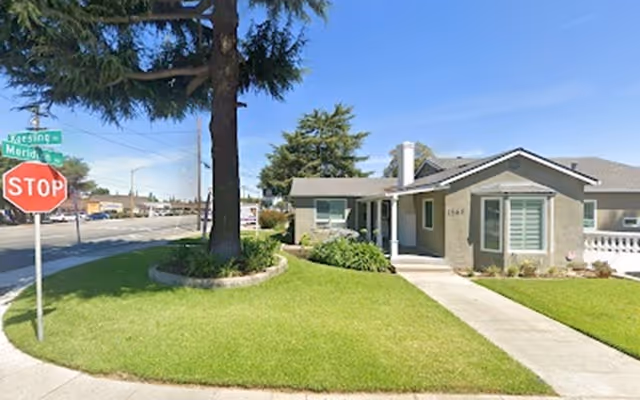 A single-story beige senior living house with a manicured lawn and stop sign.