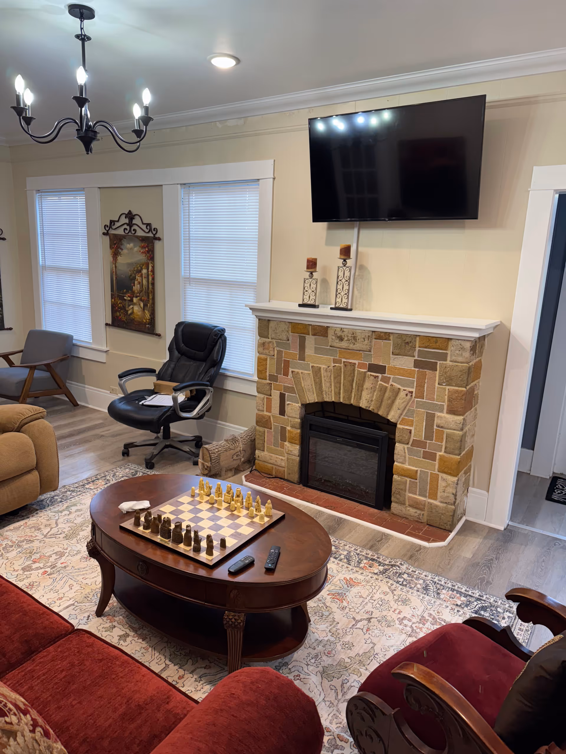 Cozy living room with stone fireplace, mounted TV, chessboard, and red seating.