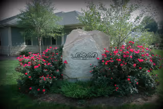 Stone sign with Willowbrook Memory Care surrounded by pink flowering bushes at the building entrance.