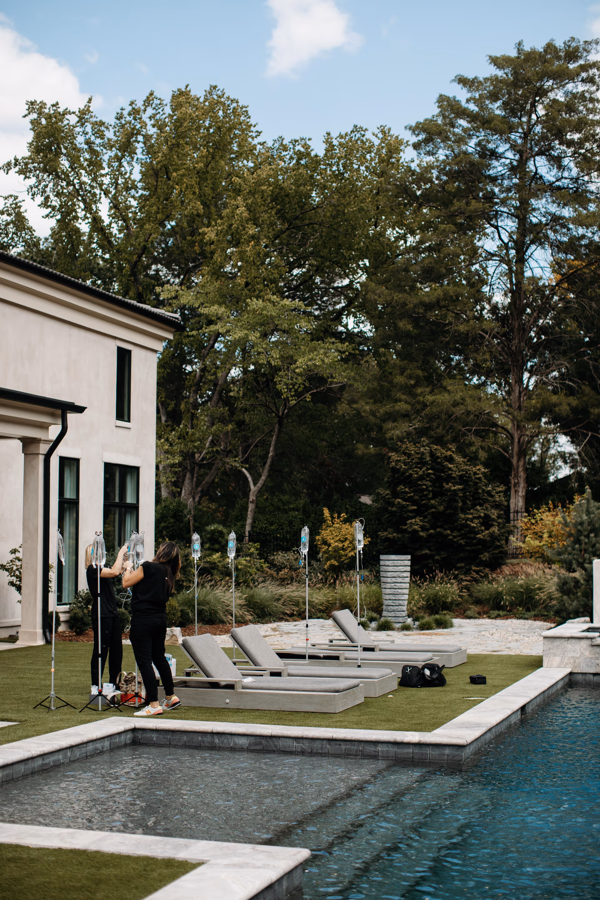 Outdoor poolside area with lounge chairs and a person setting up equipment near a building.