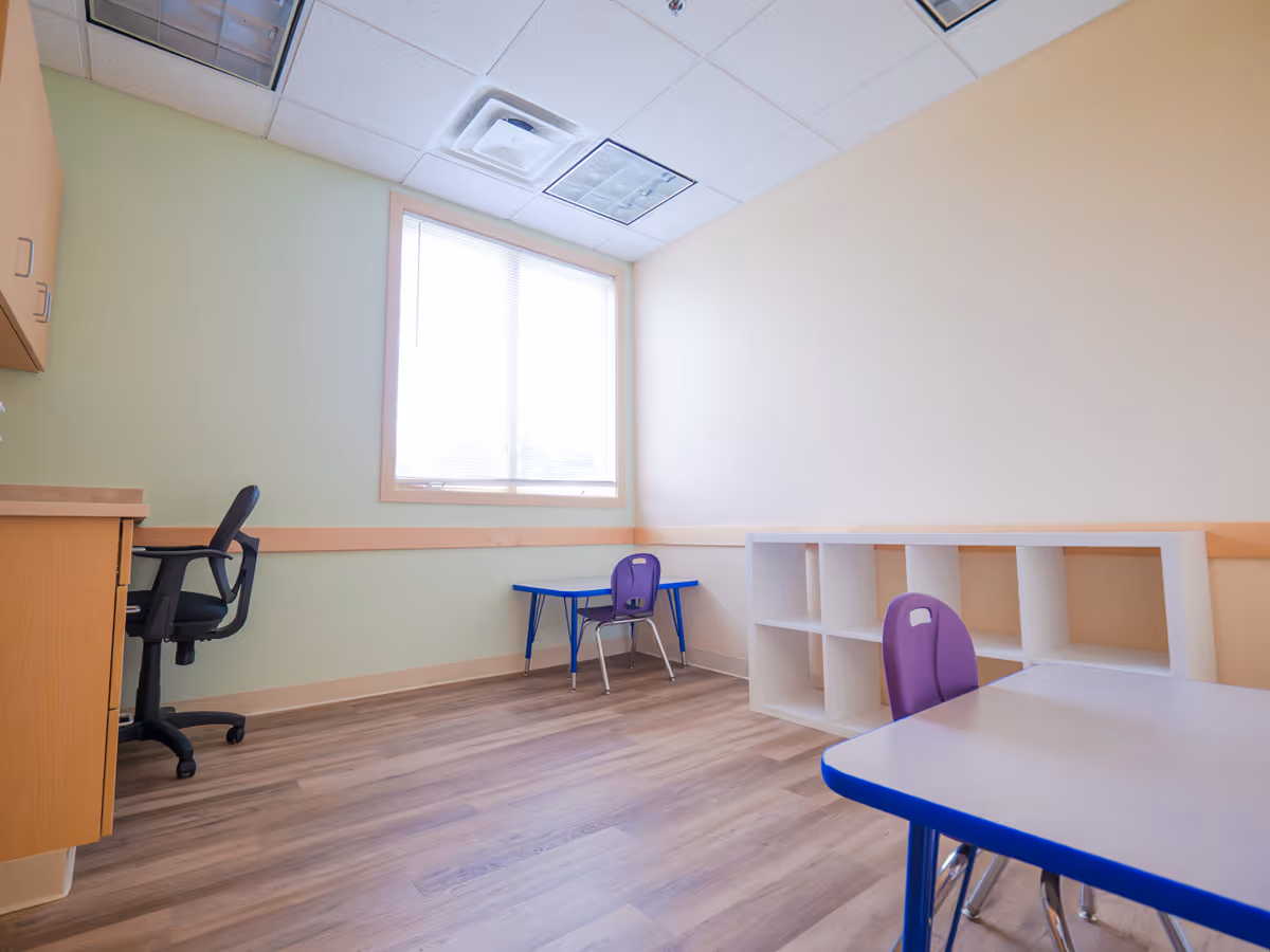 Empty classroom-style room with purple chairs, cubbies, and a windowed desk area.