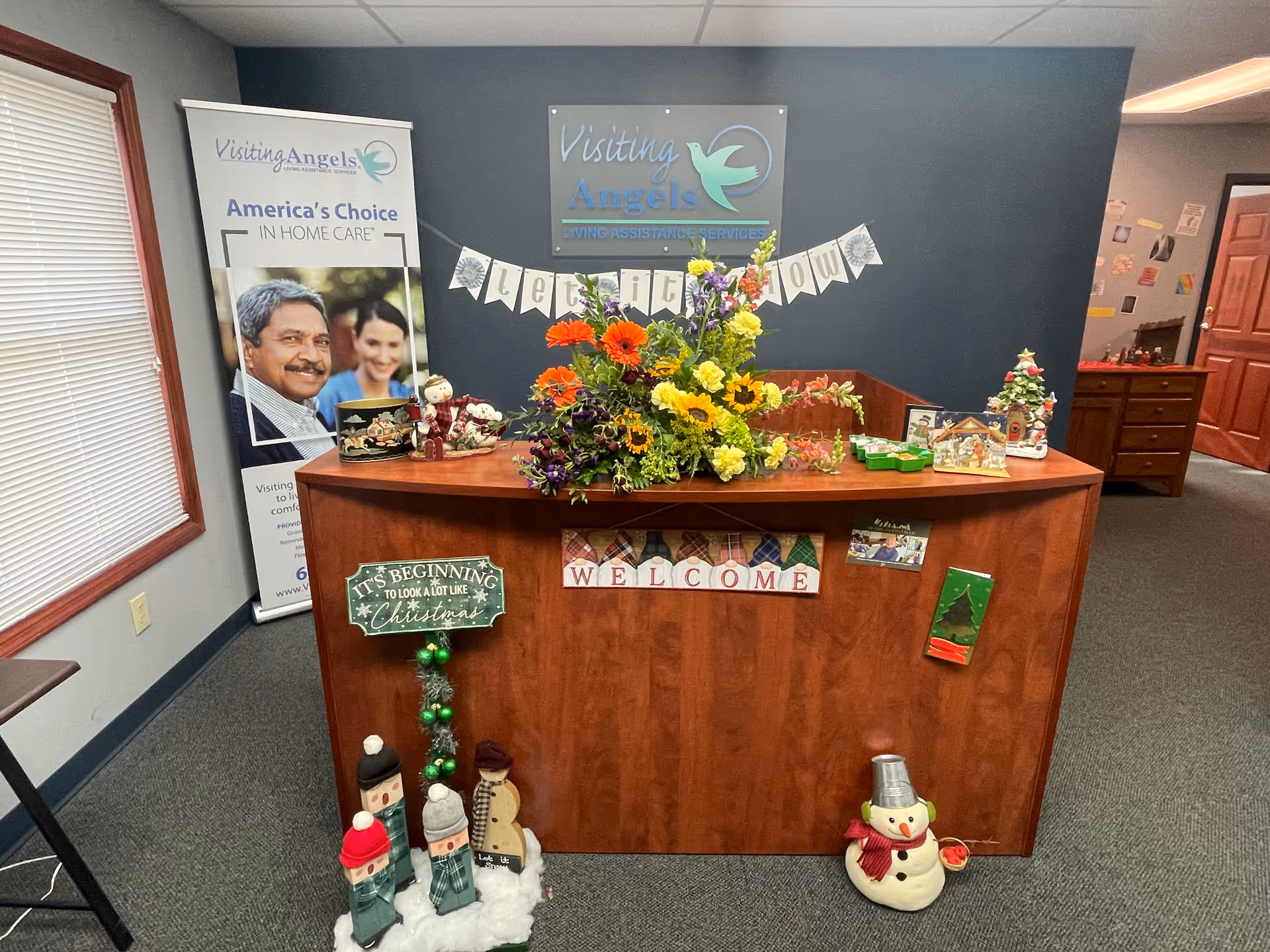 Reception desk with flowers, banners, and holiday decorations inside a Visiting Angels lobby.