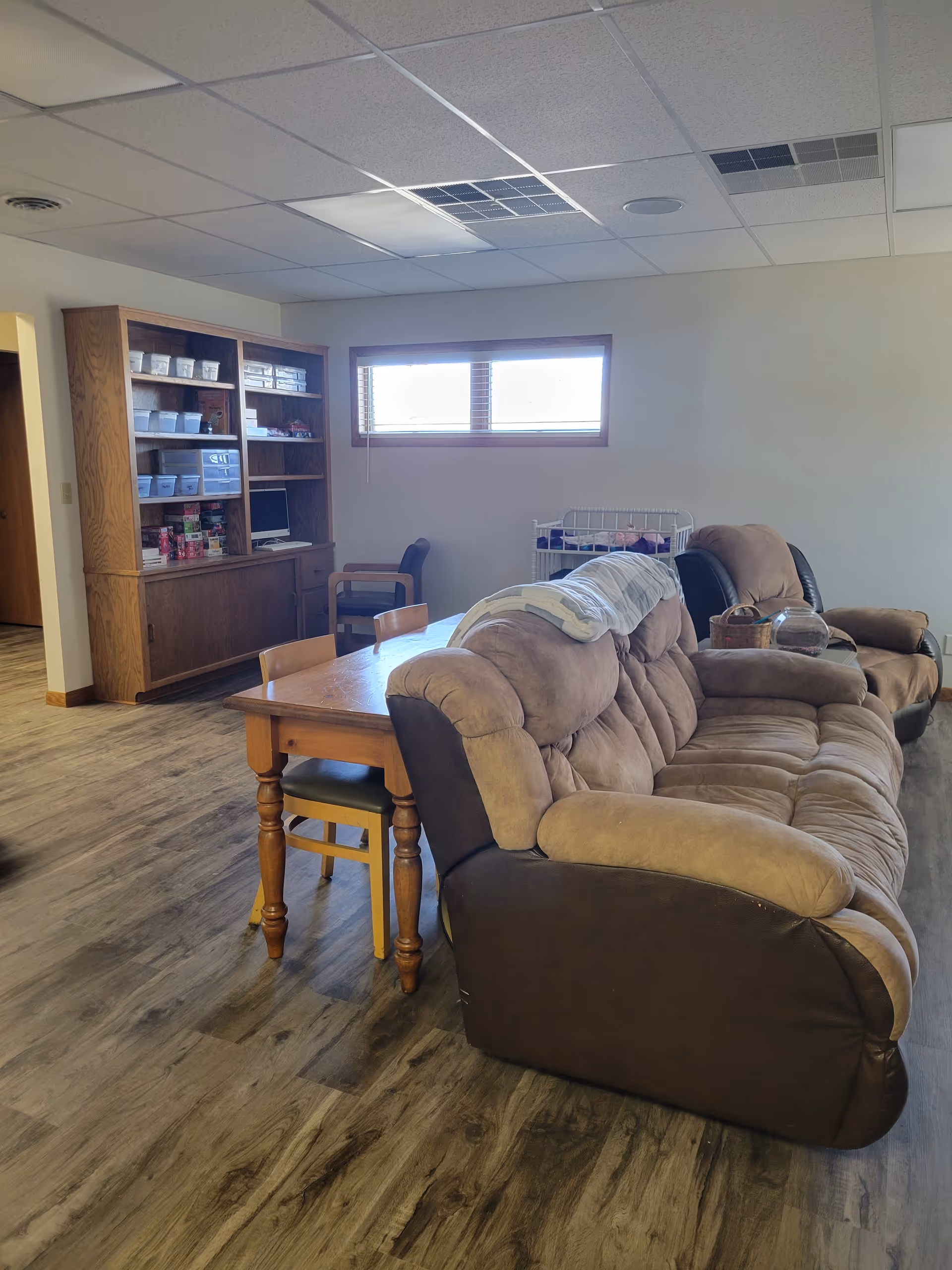 Cozy lounge area with brown sectional sofa, wooden table, and cabinet shelves.