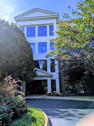 Front view of a multi-story white facility building surrounded by trees and a curved driveway.