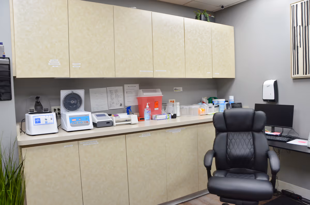 A clinical workspace with beige cabinets, counter, lab equipment, and a black chair.