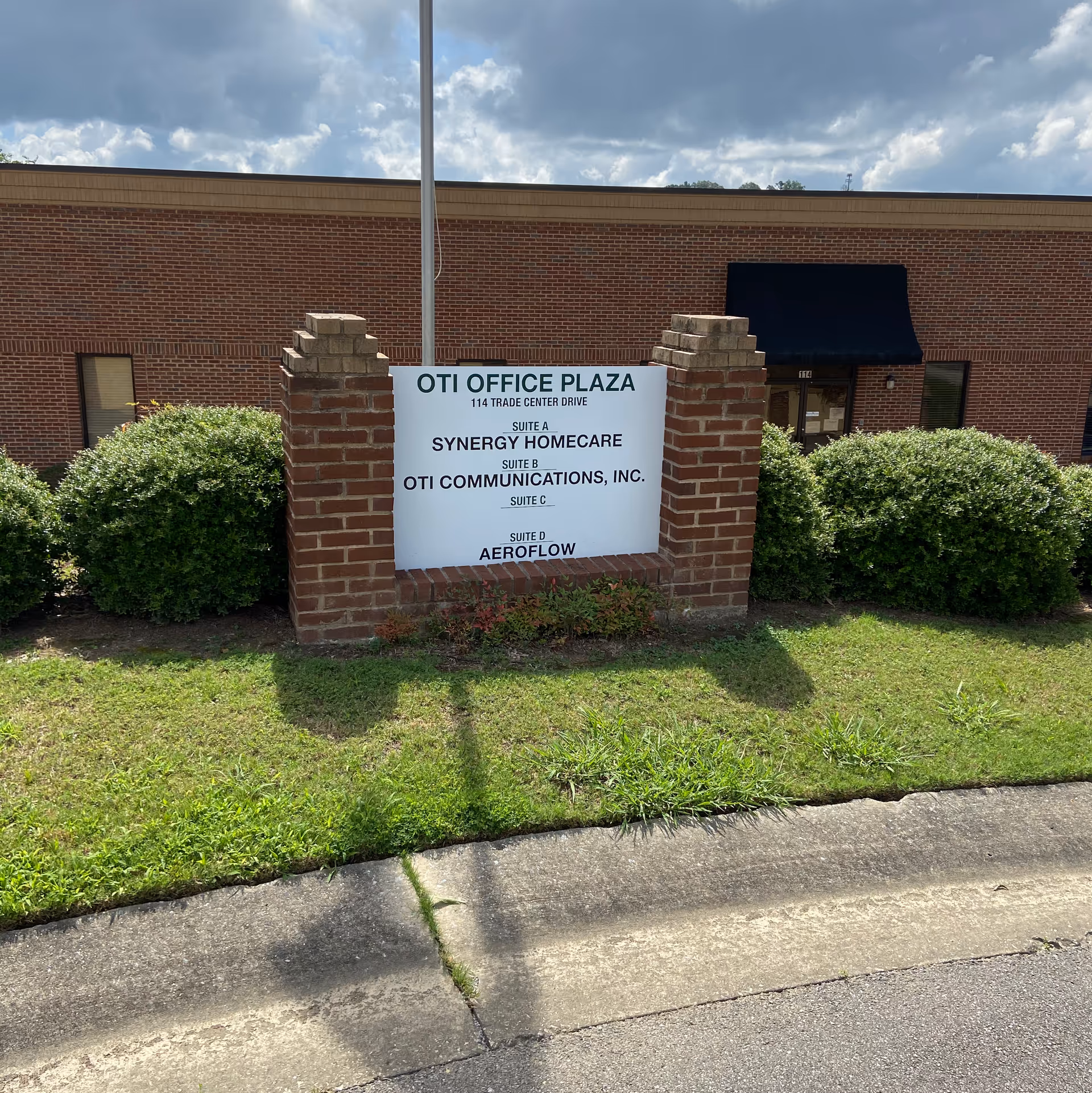 Brick sign structure reading OTI Office Plaza with Synergy HomeCare in front yard.