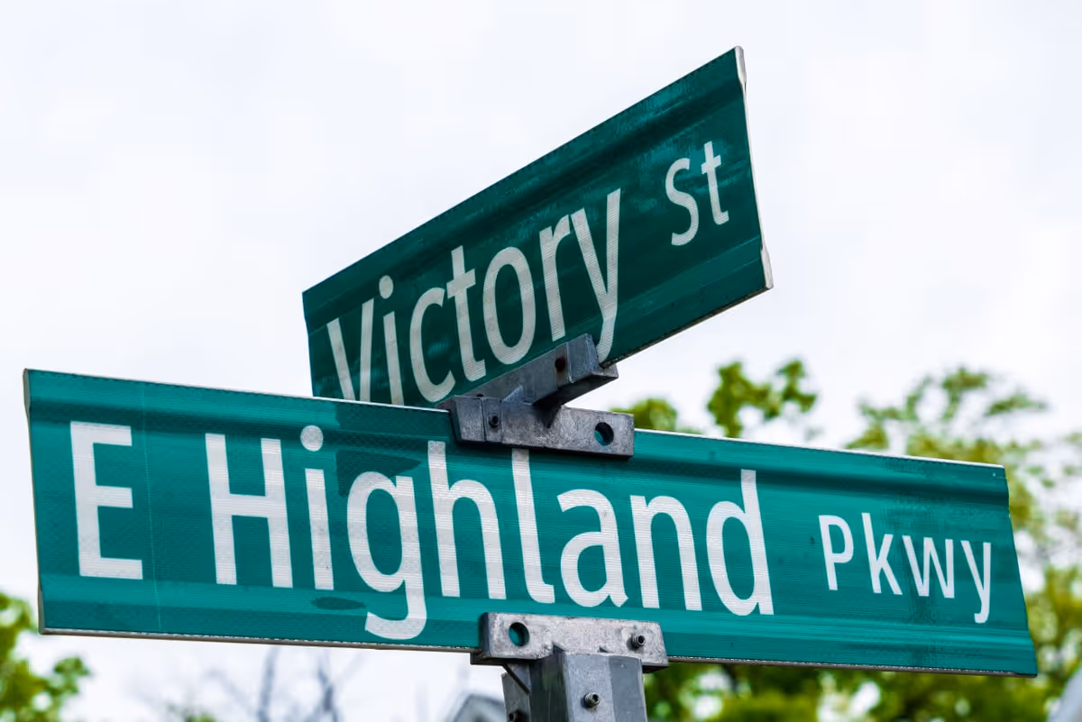 Two green street signs intersect at Victory St and E Highland Pkwy.