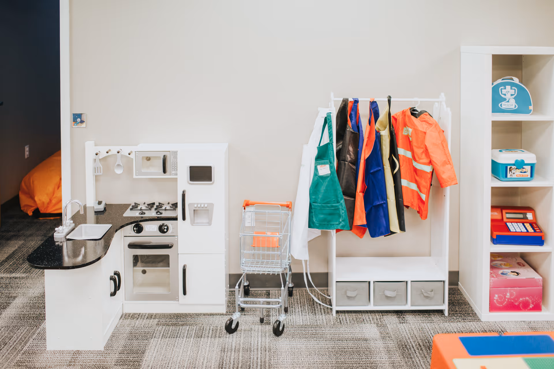 Interior playroom with a toy kitchen, coat rack, shopping cart, and cubby storage.
