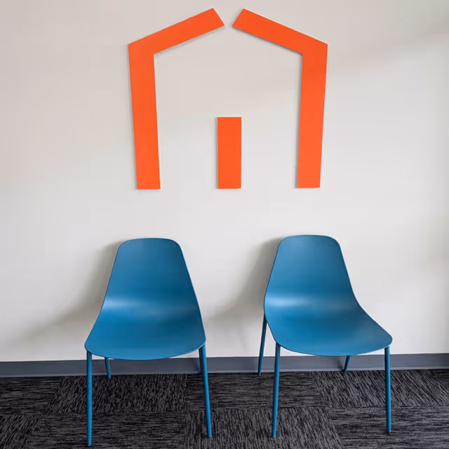 Two blue chairs sit before a white wall with an orange geometric logo.