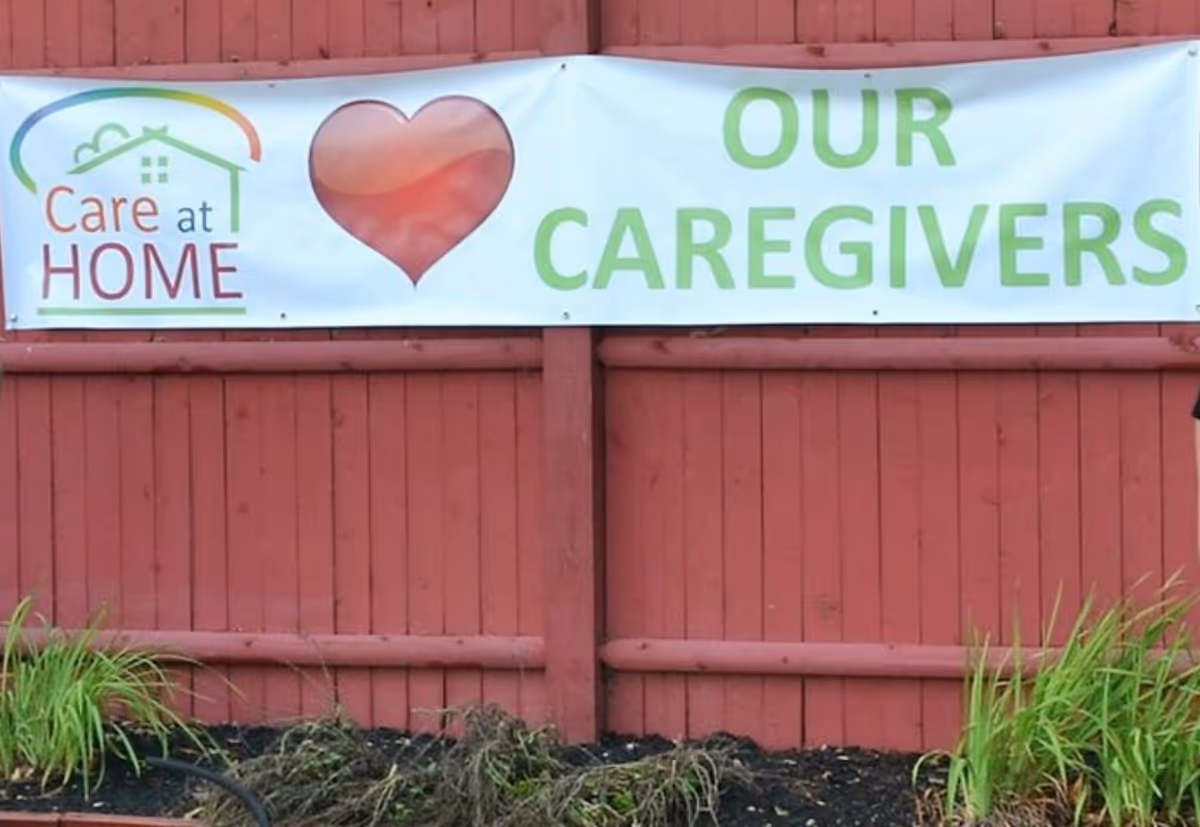 Banner on a red wooden fence advertising Care At Home with a heart symbol.